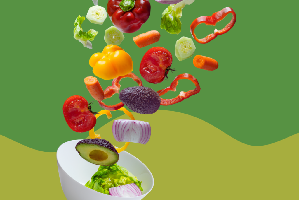 Fresh vegetables tumbling into a salad bowl against a green backdrop